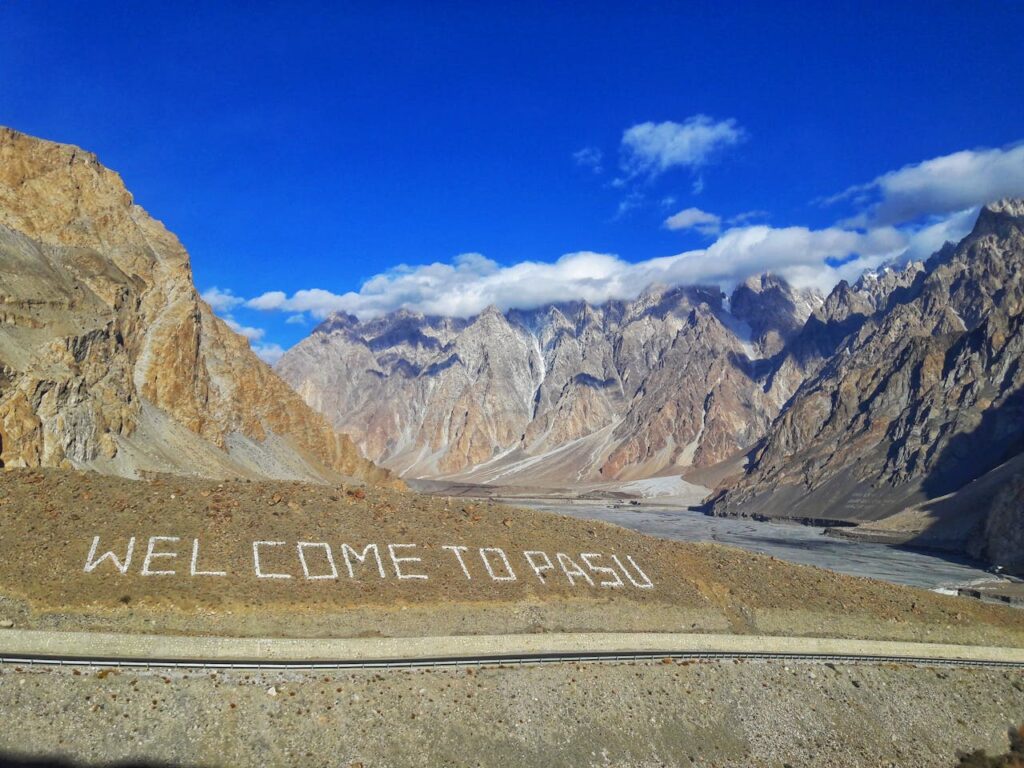 Scenic mountain landscape of Passu Cones with clear skies and welcoming text.